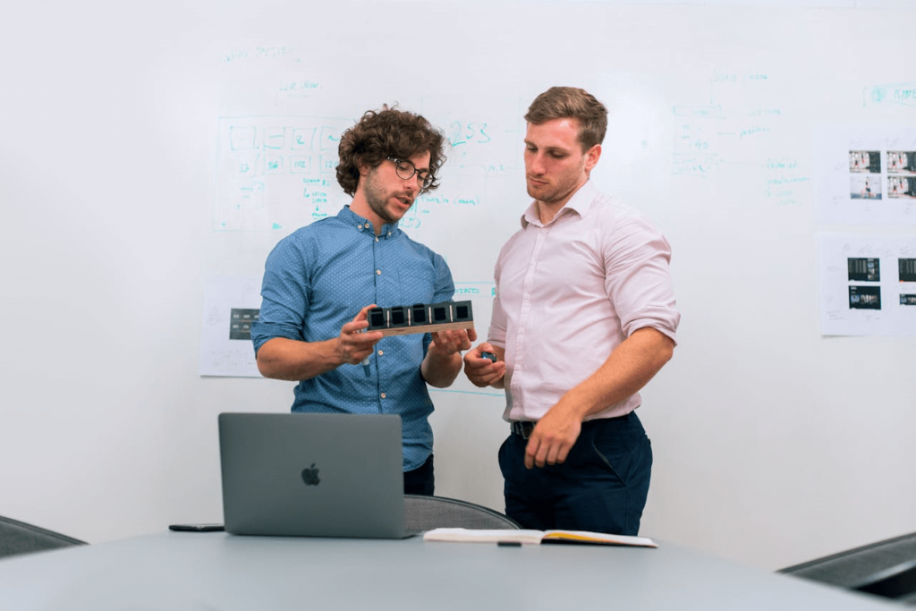 Foto van twee staande mannen die discussiëren, laptop op tafel