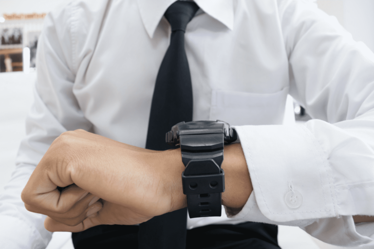 Foto van man met wit hemd en stropdas, kijkt op zijn horloge