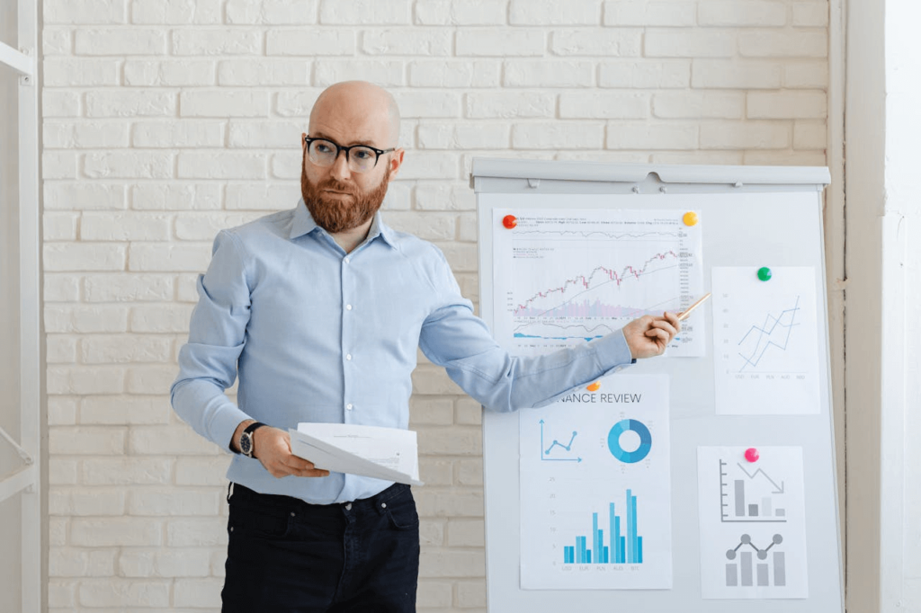 Een man die KPI’s presenteert, met behulp van grafieken en diagrammen op een flip-over om prestatietrends en bedrijfsresultaten uit te leggen.